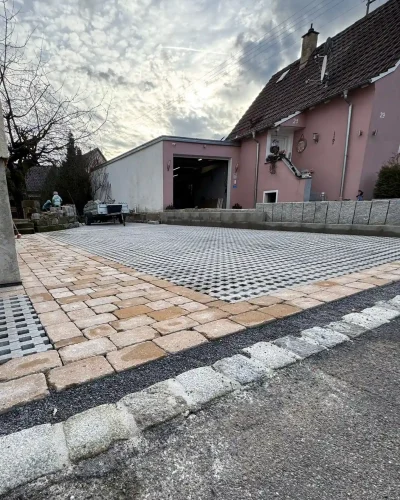 Neu gepflasterte Hofeinfahrt mit modernen Rasengittersteinen, Naturstein-Einfassung und hellen Pflastersteinen vor einem Wohnhaus