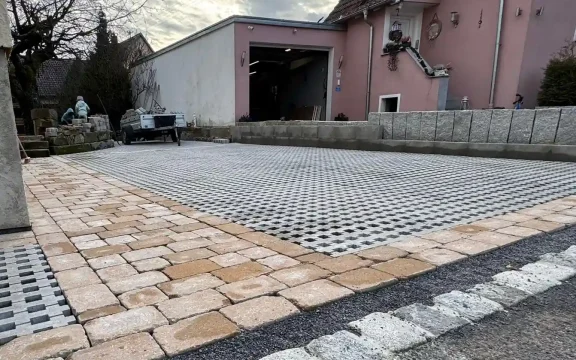 Neu gepflasterte Hofeinfahrt mit modernen Rasengittersteinen, Naturstein-Einfassung und hellen Pflastersteinen vor einem Wohnhaus